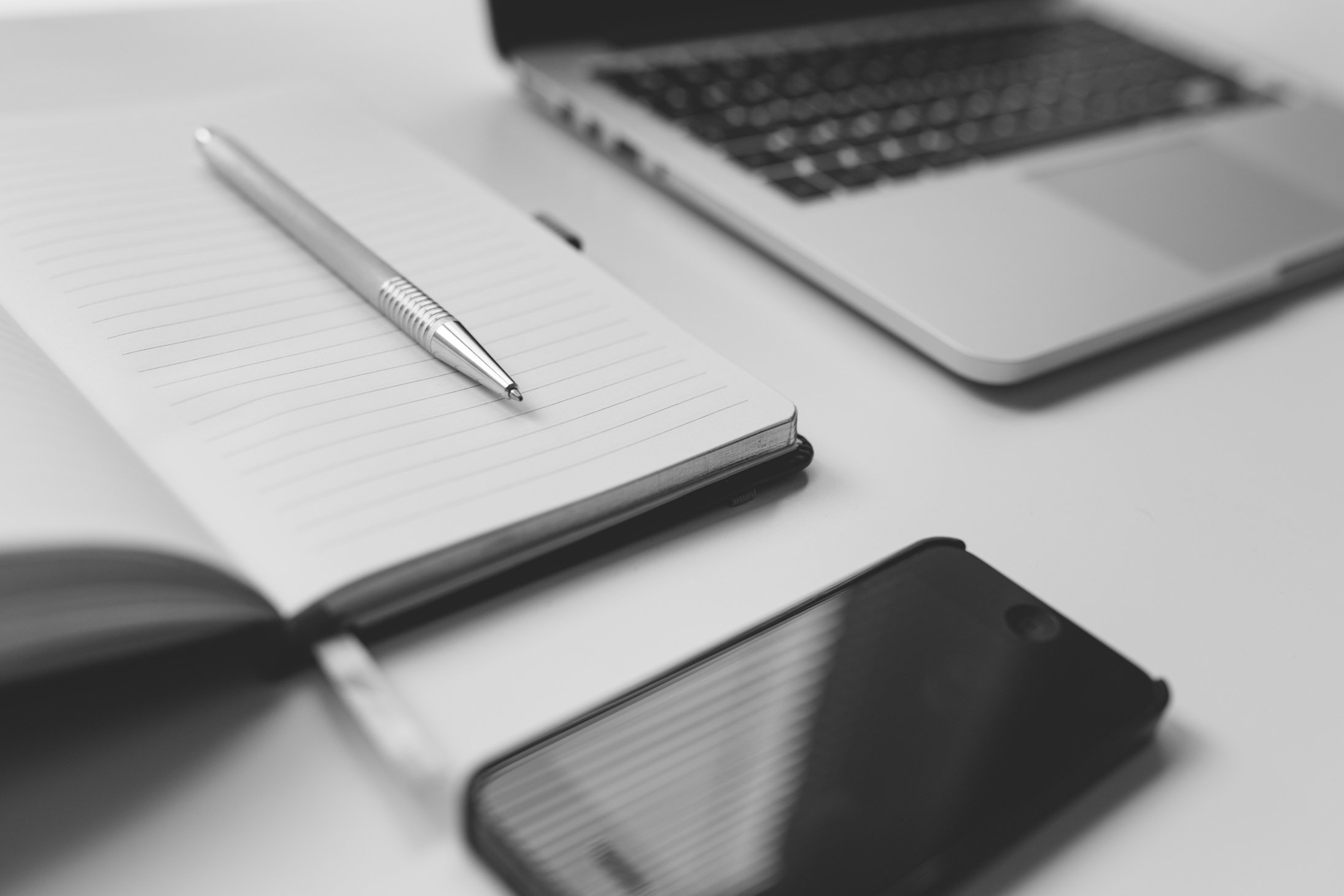 Black Iphone Beside Silver Pen on White Notebook Near Laptop Computer on Table